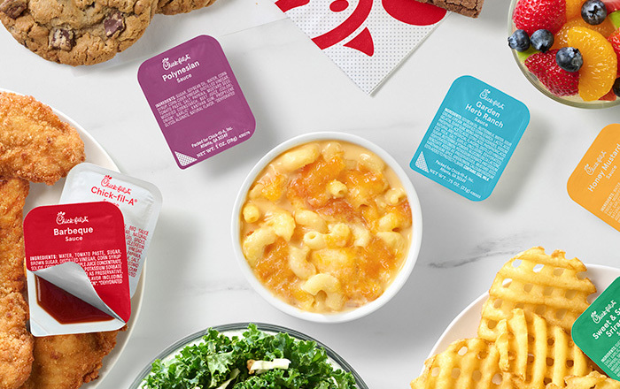 A table with Chick-n-Strips™, Mac & Cheese, Kale Crunch Side, Waffle Fries, Chocolate Chunk Cookies and Chick-fil-A sauces